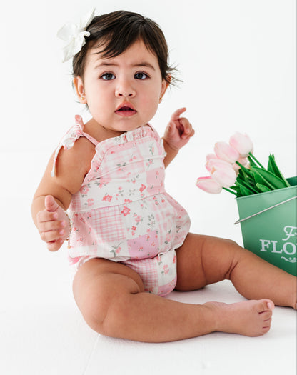 Baby in a floral bamboo bubble romper sitting next to a bucket of tulips on a white background