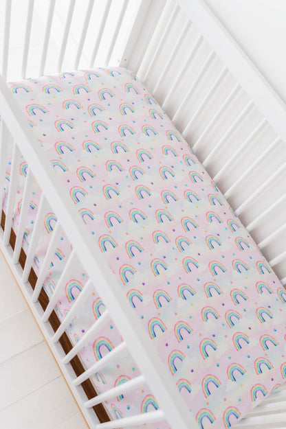 Crib with a rainbow-patterned bamboo crib sheet on a white background