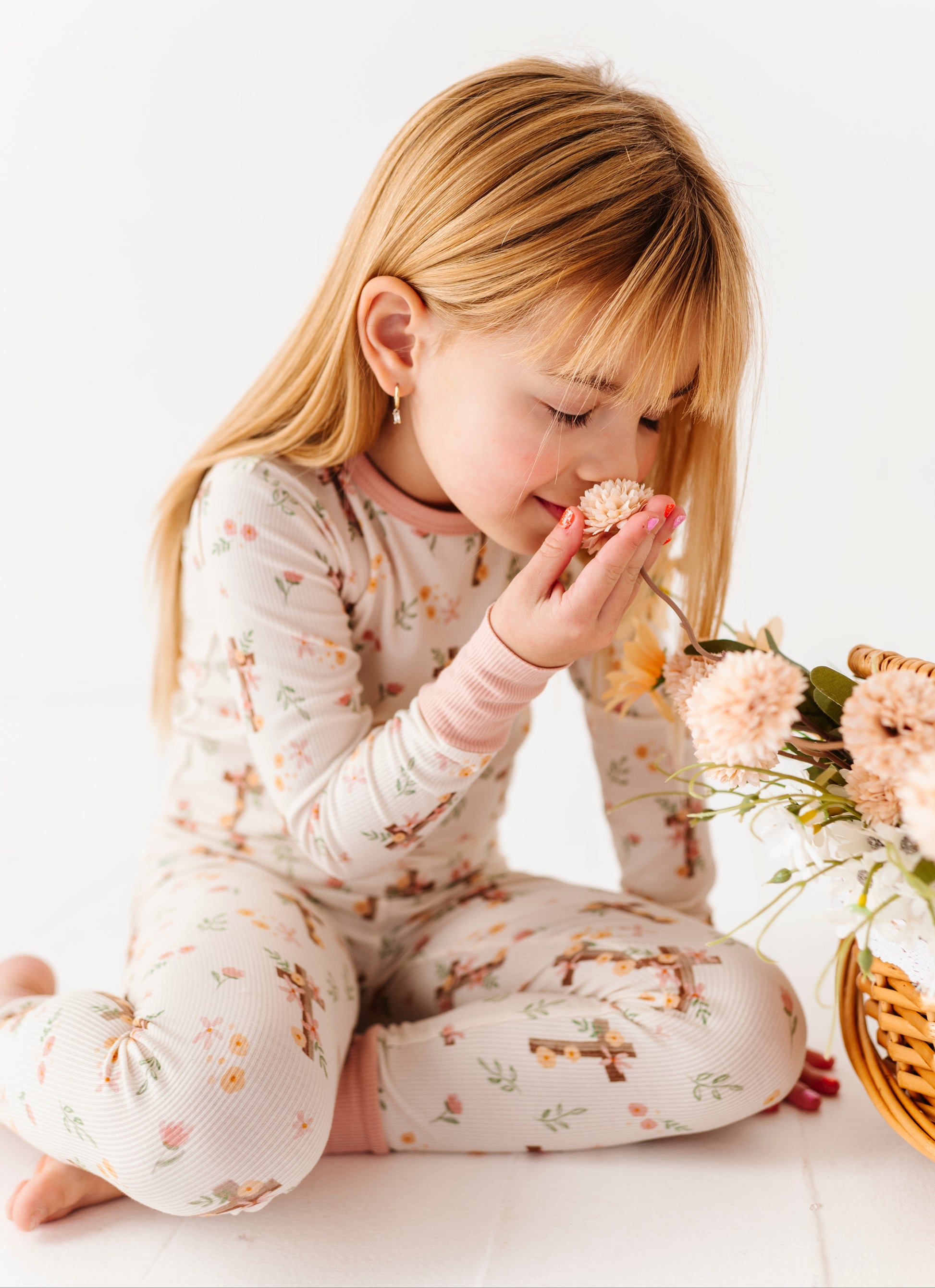 Child in bamboo pajamas smelling a flower with a basket of flowers in the background