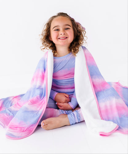 Child wrapped in a colorful tie-dye bamboo blanket, wearing matching bamboo pajamas, on a white background