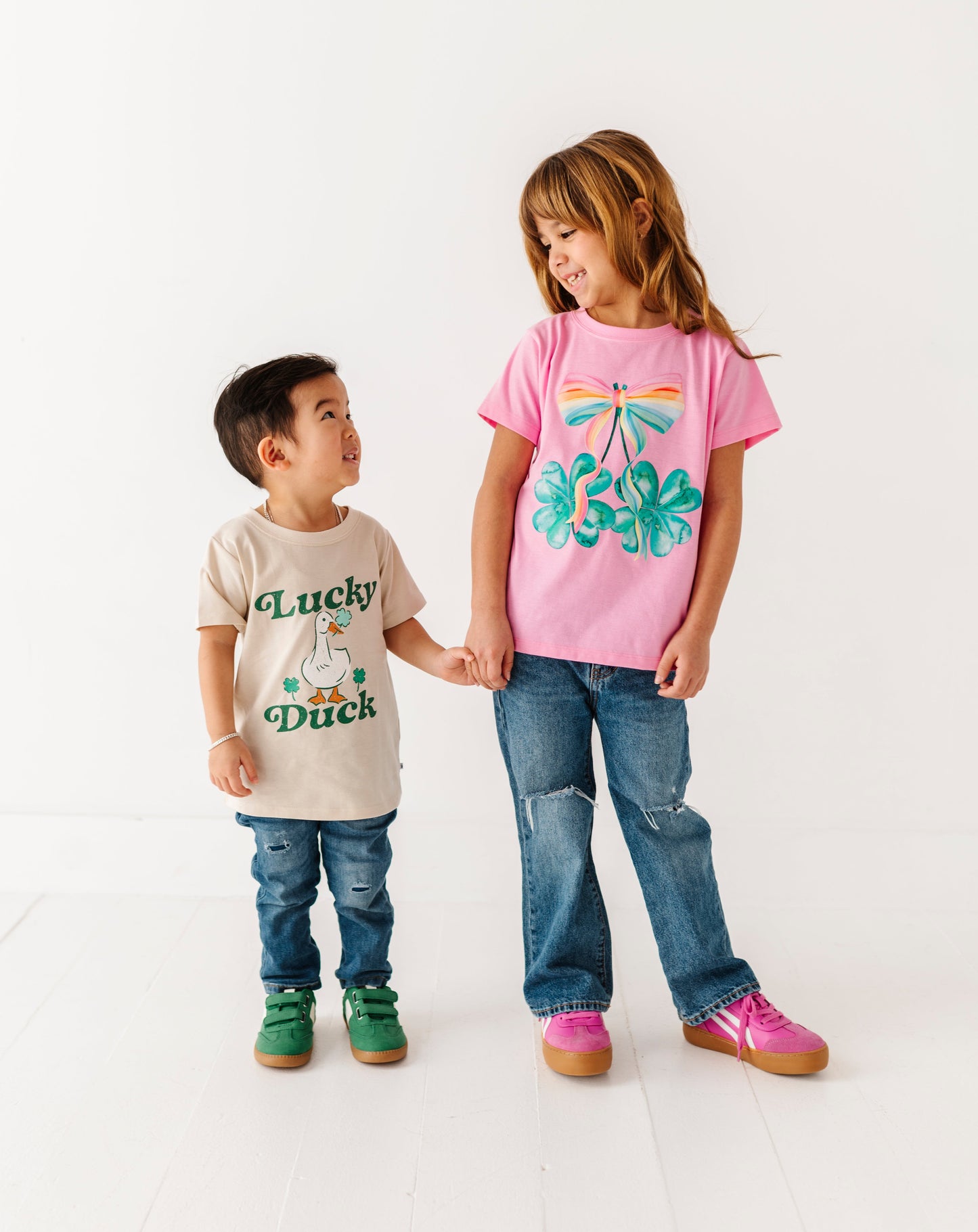 Two children standing on a white background wearing t-shirts with graphics and text.