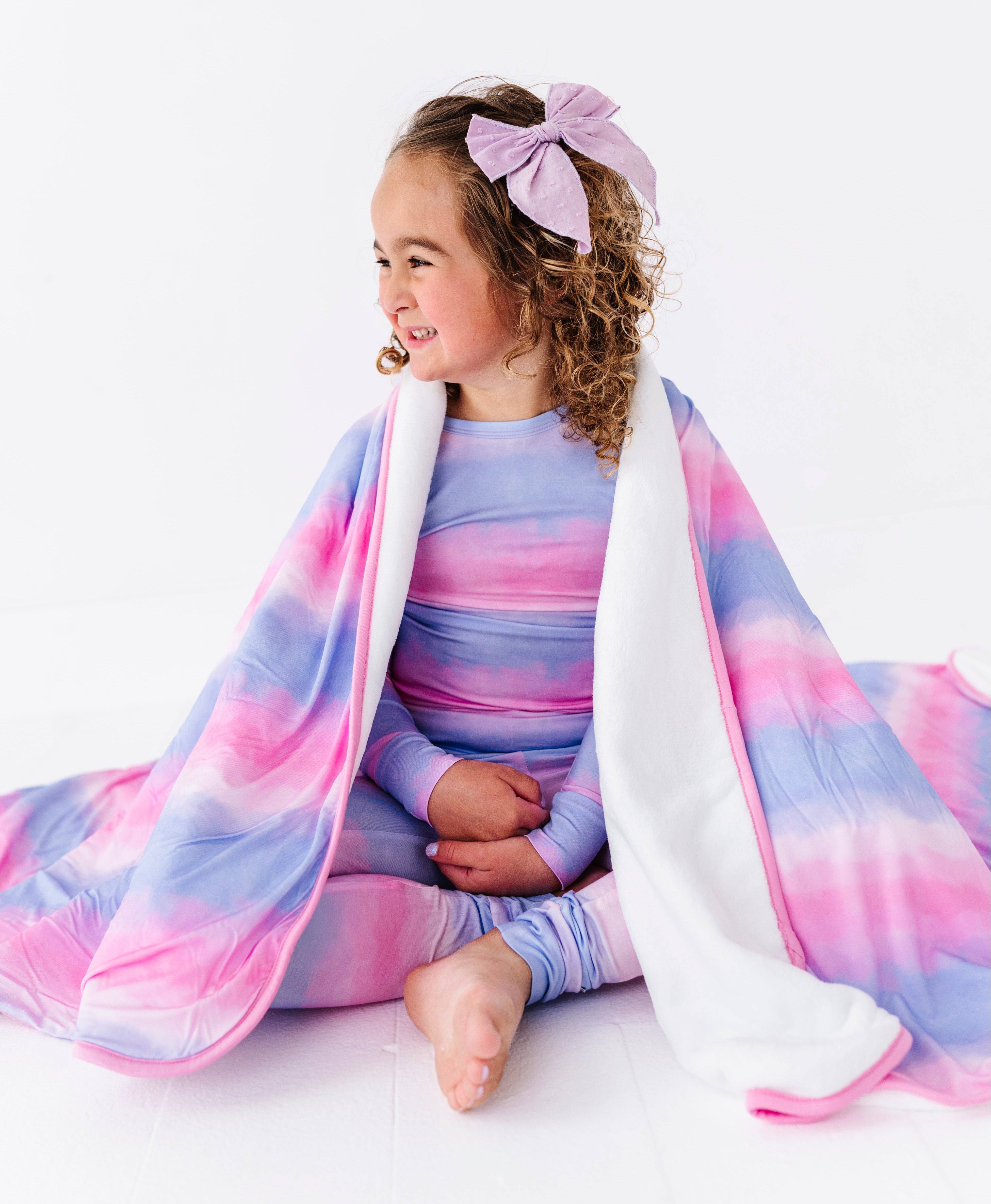 Child wrapped in a pink and purple striped bamboo blanket with a plush backing on a white background
