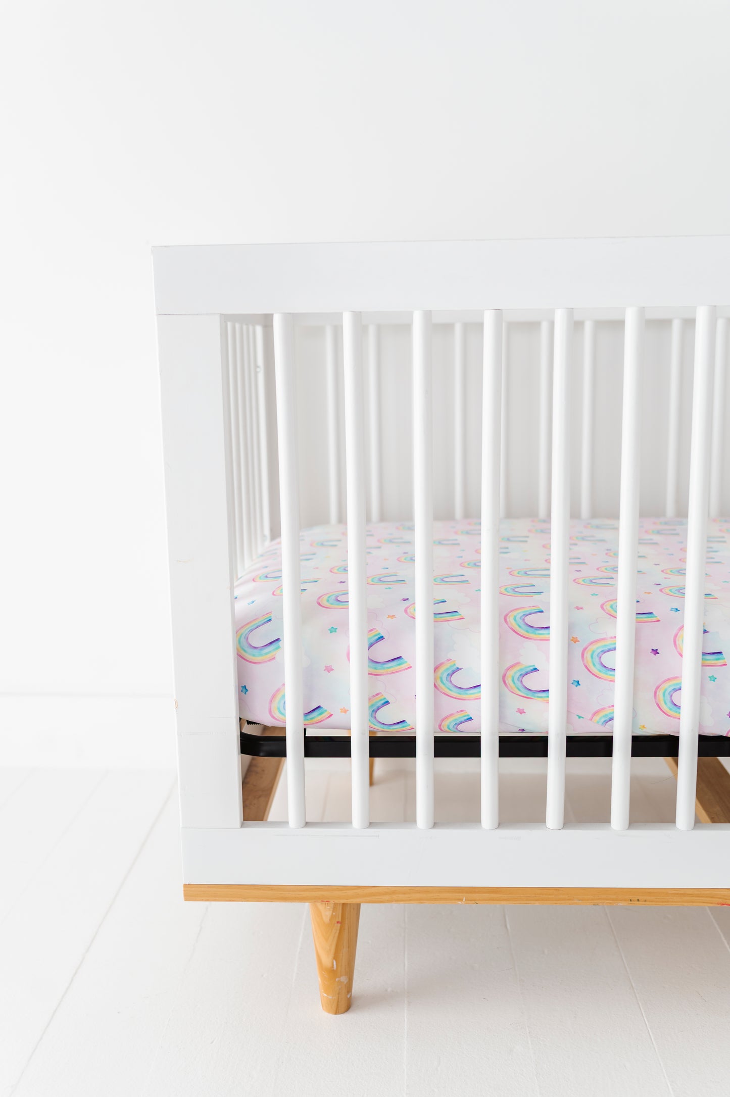 White crib with a colorful bamboo crib mattress on a white floor and wall