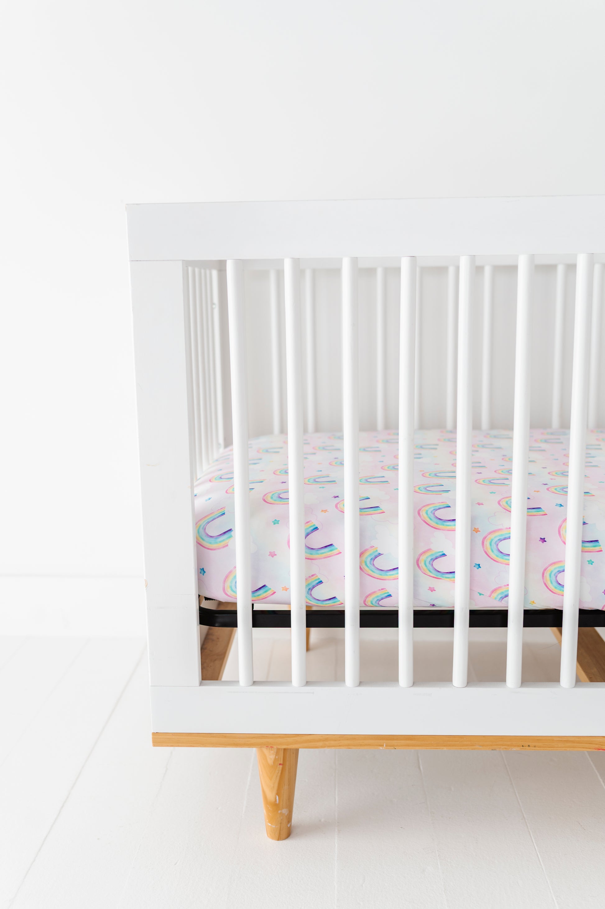 White crib with a colorful bamboo crib mattress on a white floor and wall