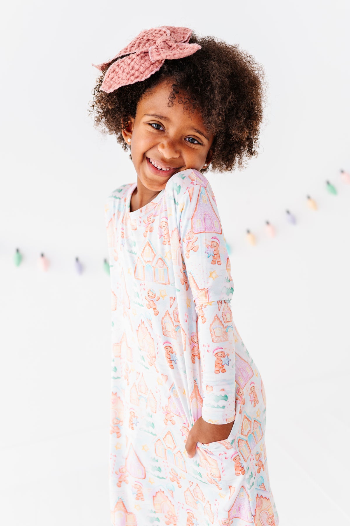 A little girl wearing a Christmas gingerbread-themed bamboo nightgown, standing in a bright white room 