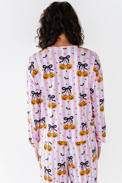 A model viewed from behind wearing a matching long-sleeve pajama set with a pink and white striped Halloween pattern featuring pumpkins, black bows, and bats.