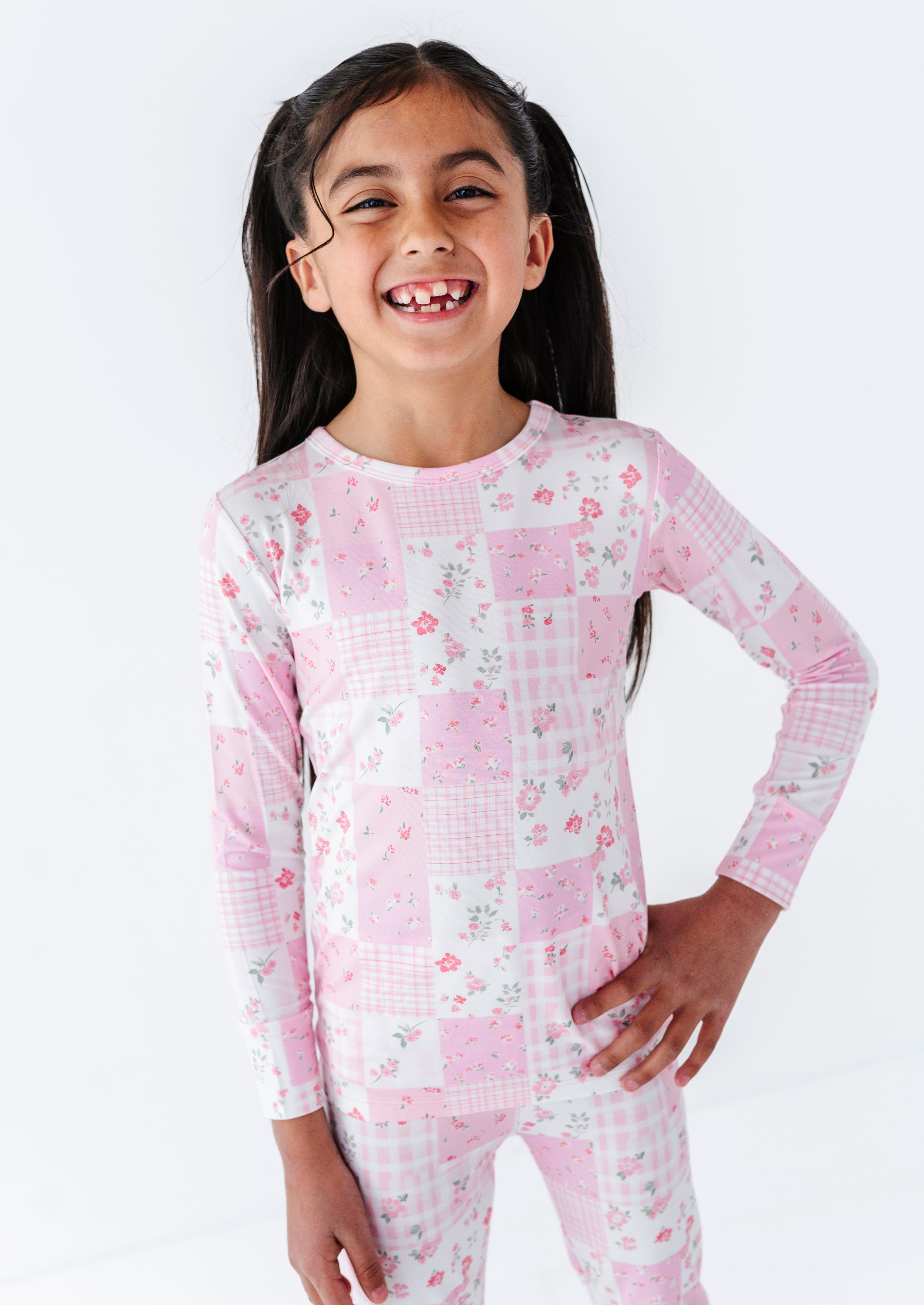 Young girl wearing a pink and white checkered bamboo two-piece pajama set with a floral pattern on a white background