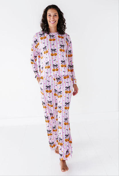 A woman modeling a long-sleeve pajama set with a Halloween pumpkin and cat print, standing against a plain white studio background.