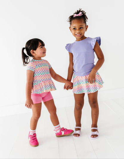 Two young girls wearing colorful bamboo outfits standing against a white background