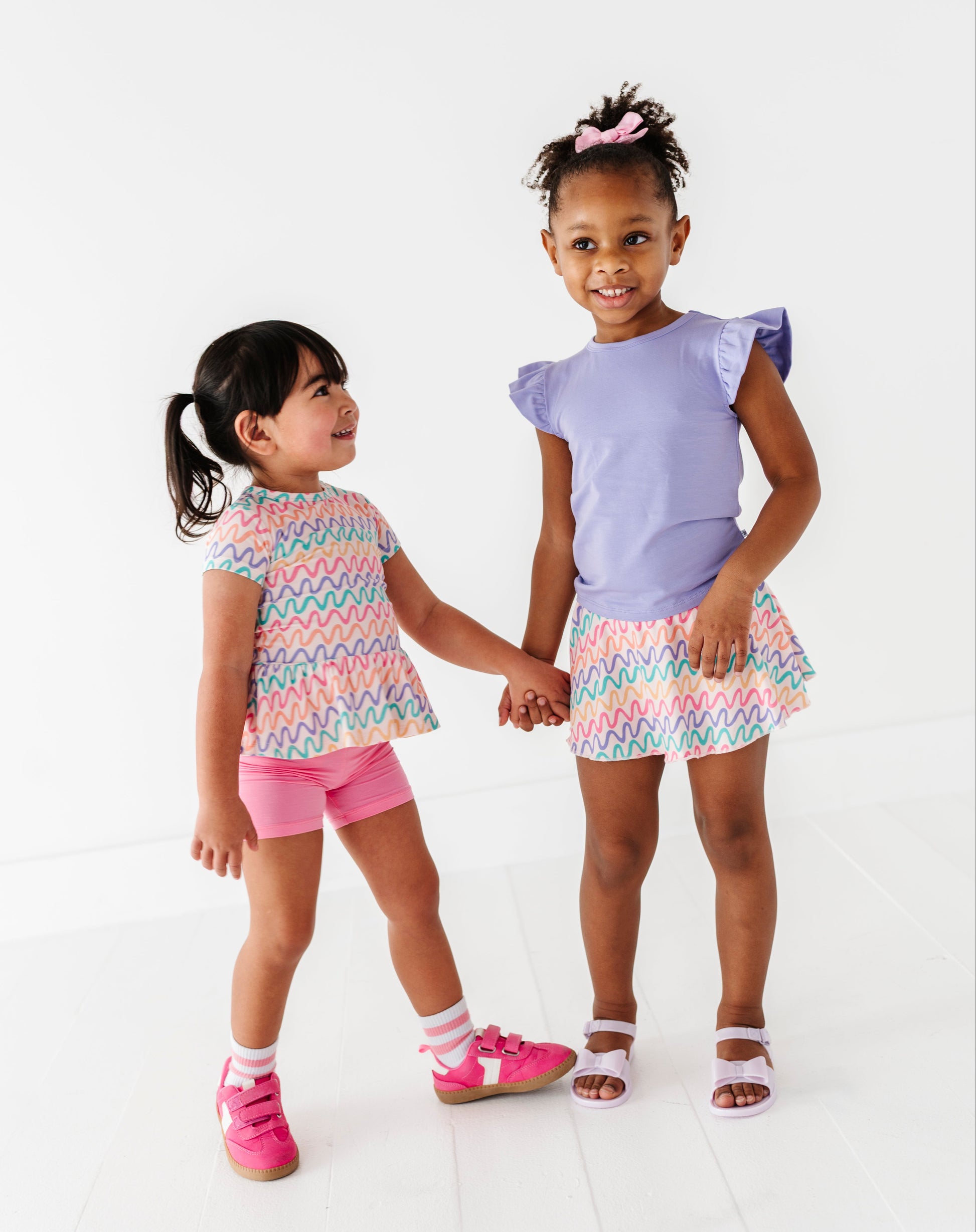 Two young girls wearing Squiggles bamboo outfits standing against a white background