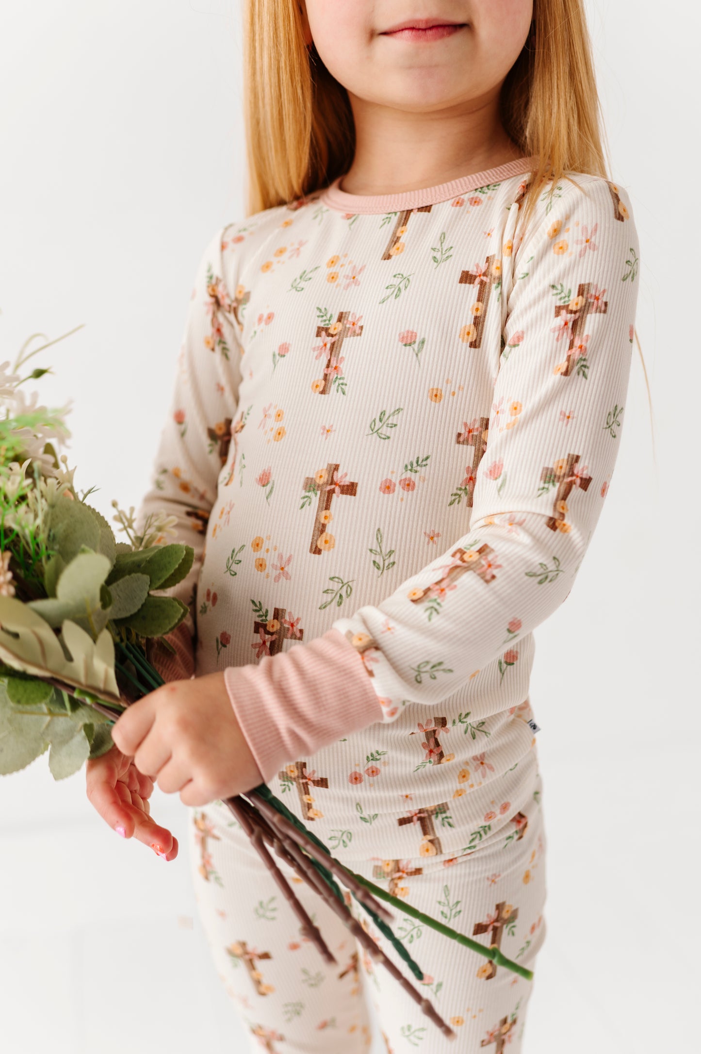 Child wearing a bamboo long-sleeve pajama set with cross patterns holding flowers on a white background