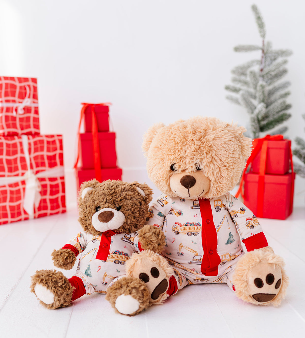Two teddy bears sitting in a bright white room wearing matching construction-themed doll rompers.