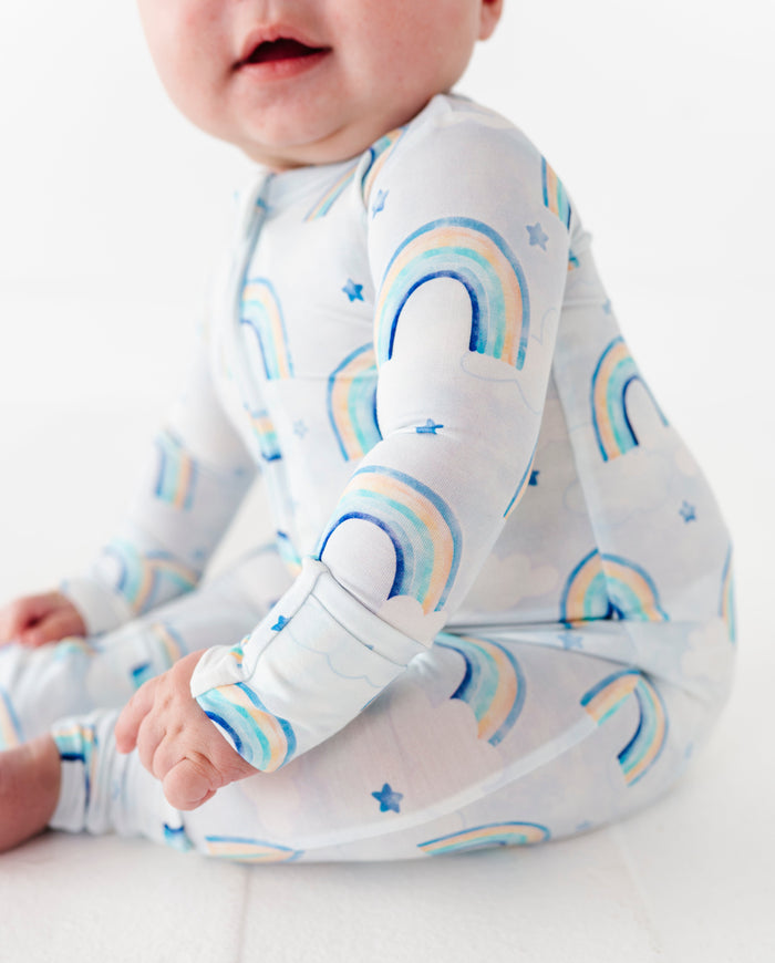 Baby wearing a bamboo zip romper with watercolor rainbow pattern on a white background
