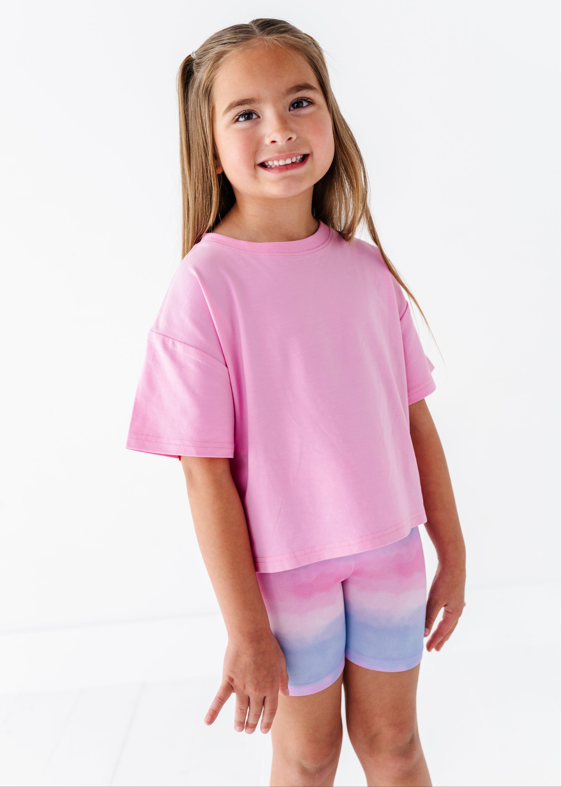 Young girl wearing a pink bamboo-cotton shirt and colorful bamboo biker shorts on a white background