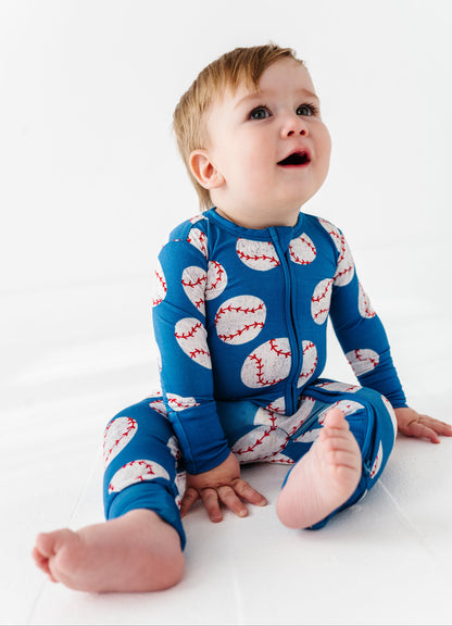 Baby wearing a blue convertible romper with white baseball patterns on a white background