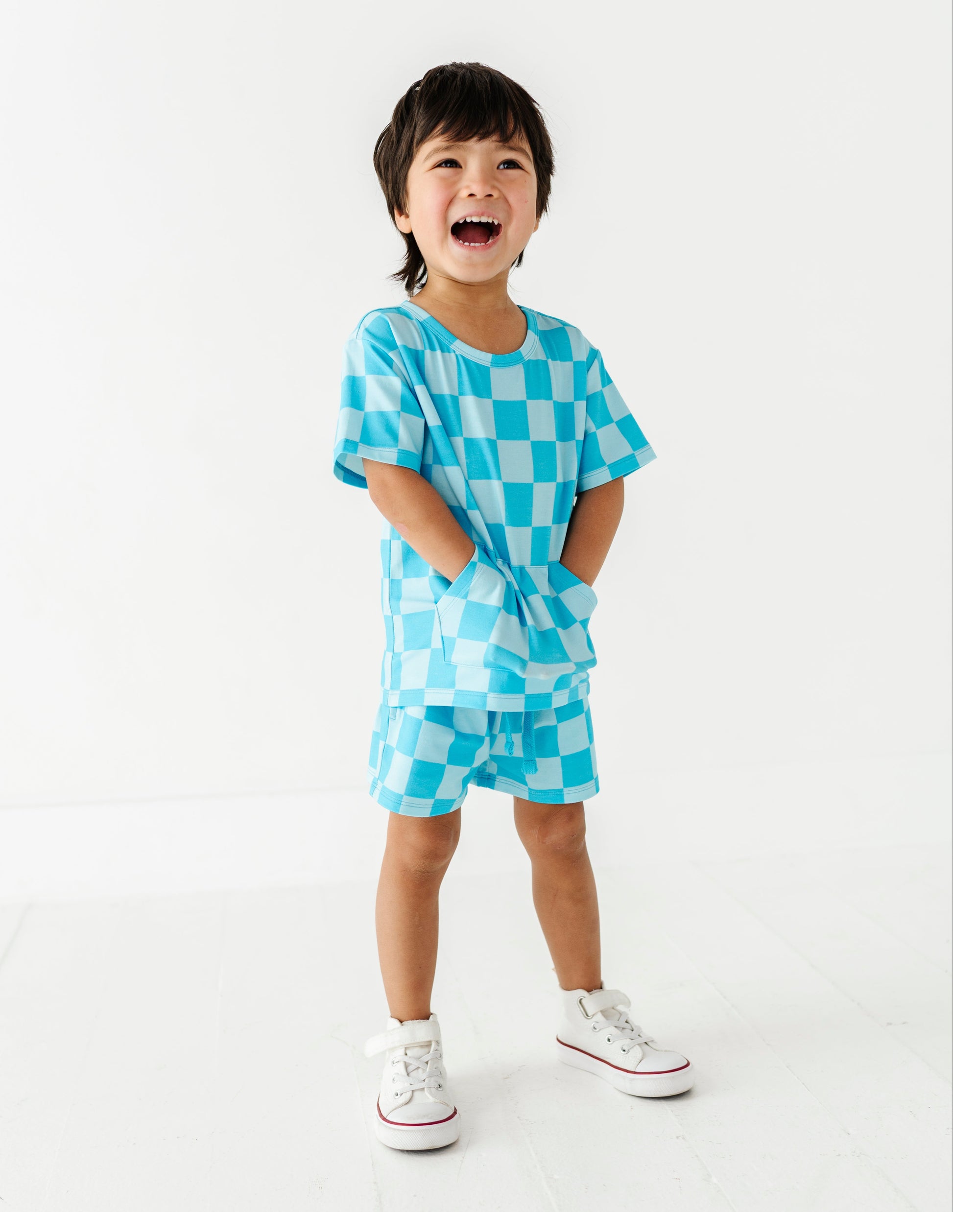 A young child wearing a matching light blue checkered short-sleeve t-shirt and shorts set, standing against a clean white studio background.