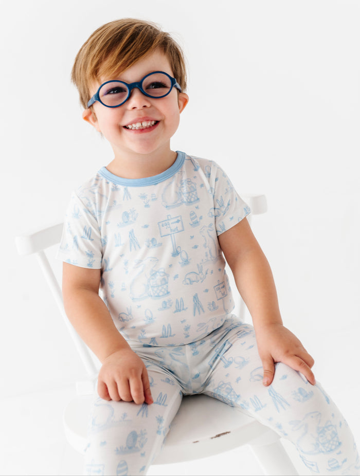 Child wearing glasses and a light blue Easter pajama set with animal prints on a white background
