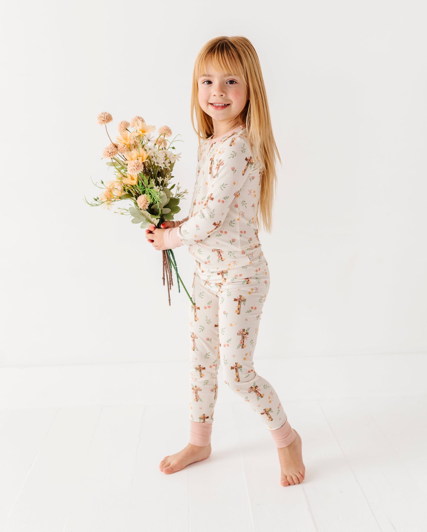 Young girl in a floral bamboo two-piece set holding flowers on a white background
