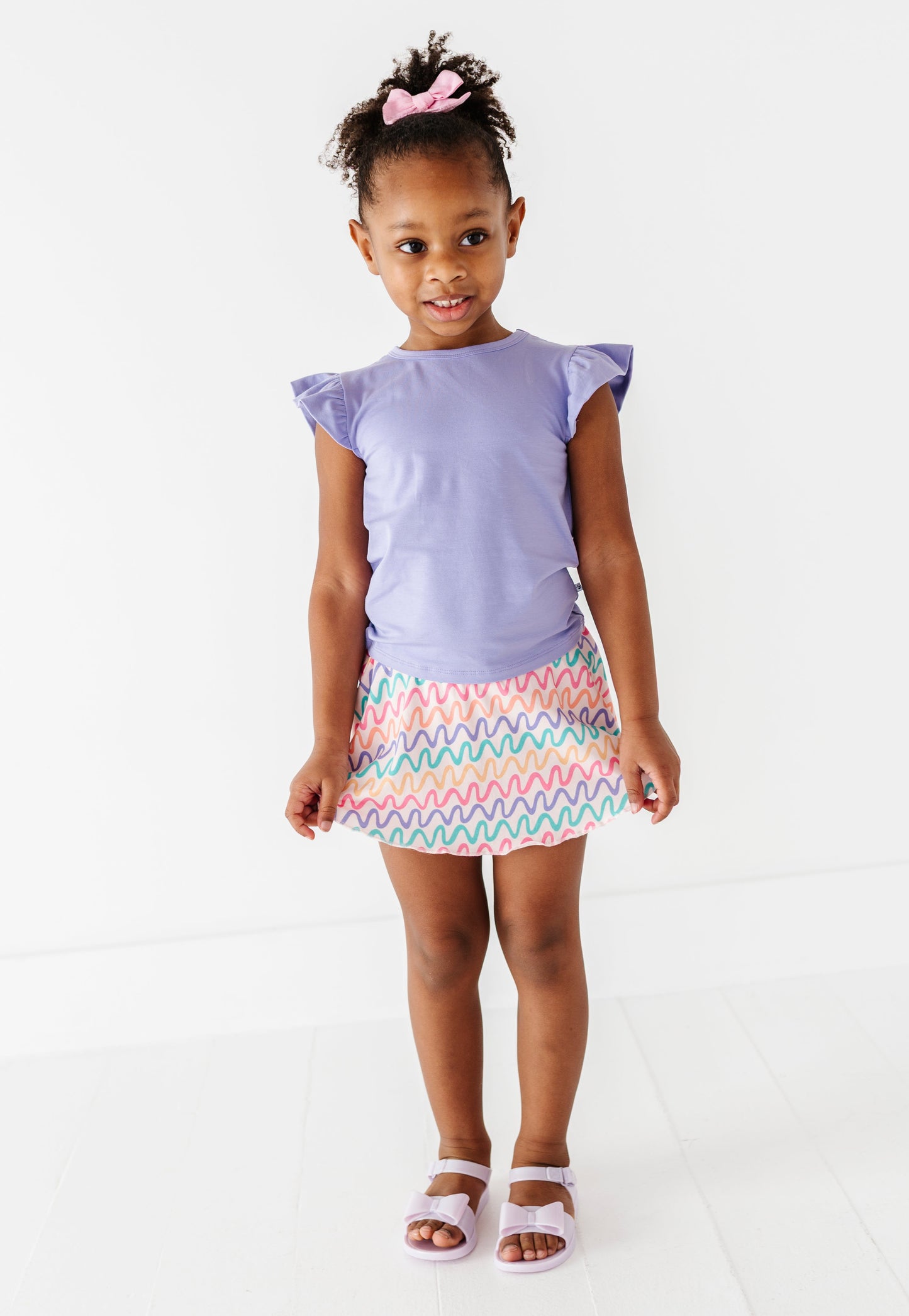 Young girl wearing a purple bamboo/cotton top and colorful bamboo skort on a white background