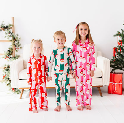 Three kids posed together in front of Christmas decor. They're wearing coordinating bamboo pajamas in pink stripe, red stripe, and green stripe 