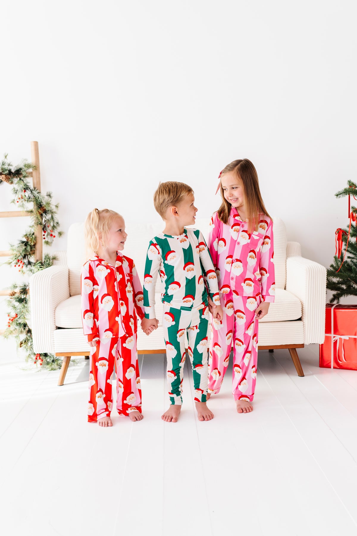 Three children wearing coordinating bamboo pajama sets featuring Santa Claus stripes 
