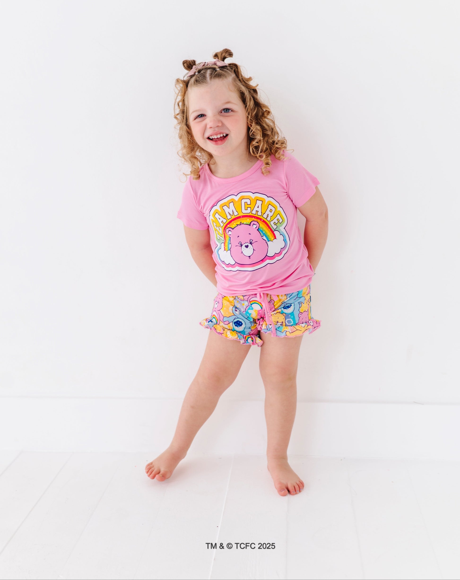 Child wearing pink Care Bears™ “Team Care” t-shirt with rainbow graphic and matching Care Bears print lounge shorts