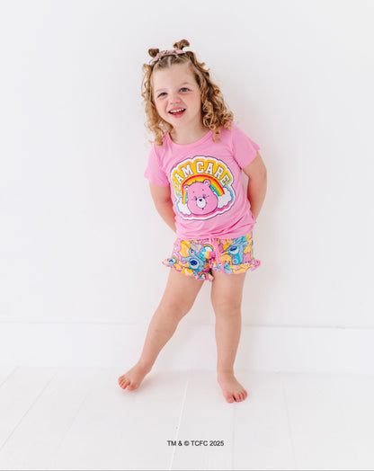 Child wearing pink Care Bears™ “Team Care” t-shirt with rainbow graphic and matching Care Bears print lounge shorts