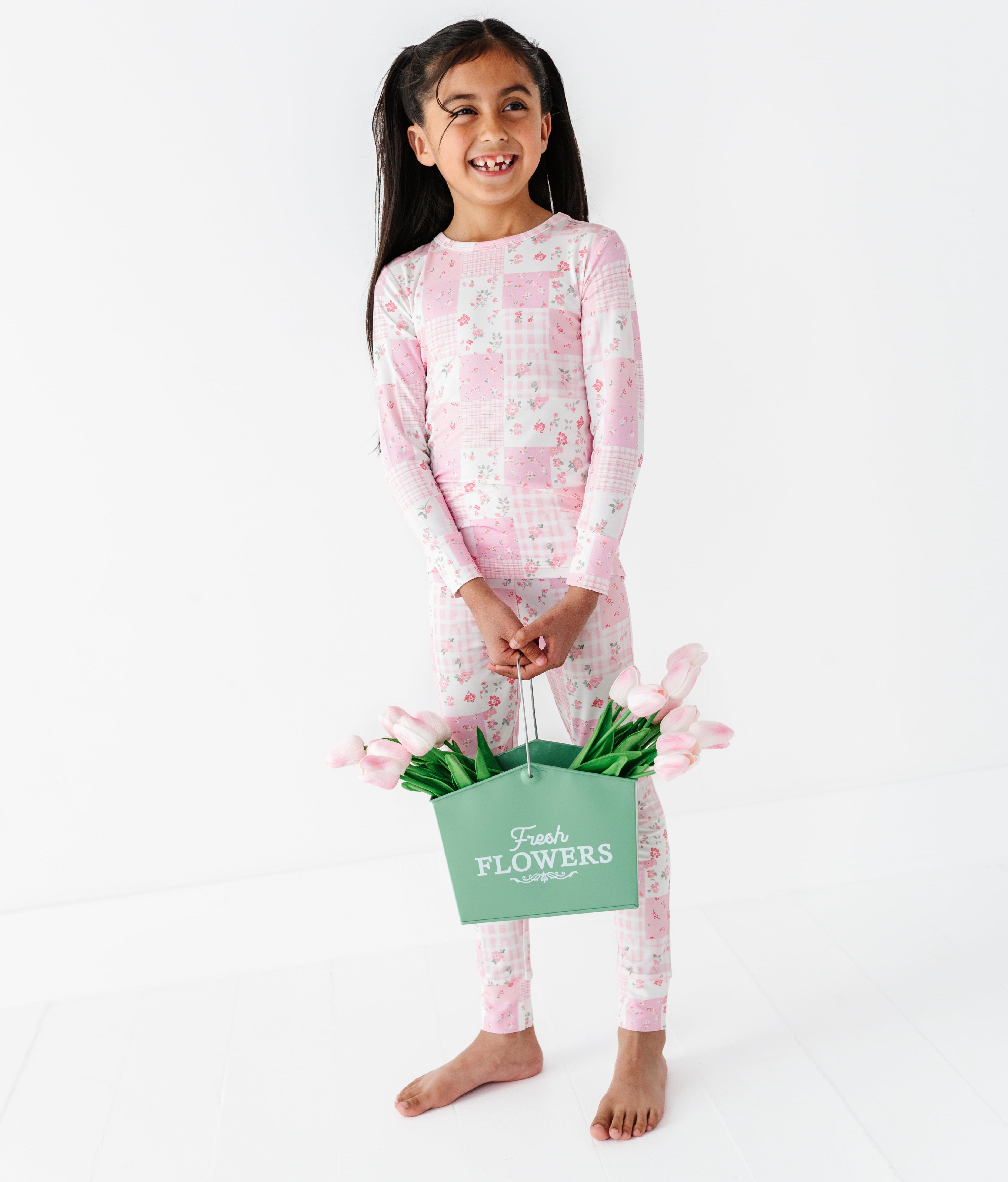 Young girl in pink floral bamboo two-piece pajamas holding a basket of flowers on a white background