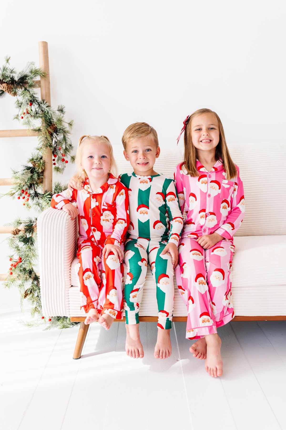 Siblings wearing coordinating St. Nick Stripes bamboo pajamas in red, green, and pink for Christmas 