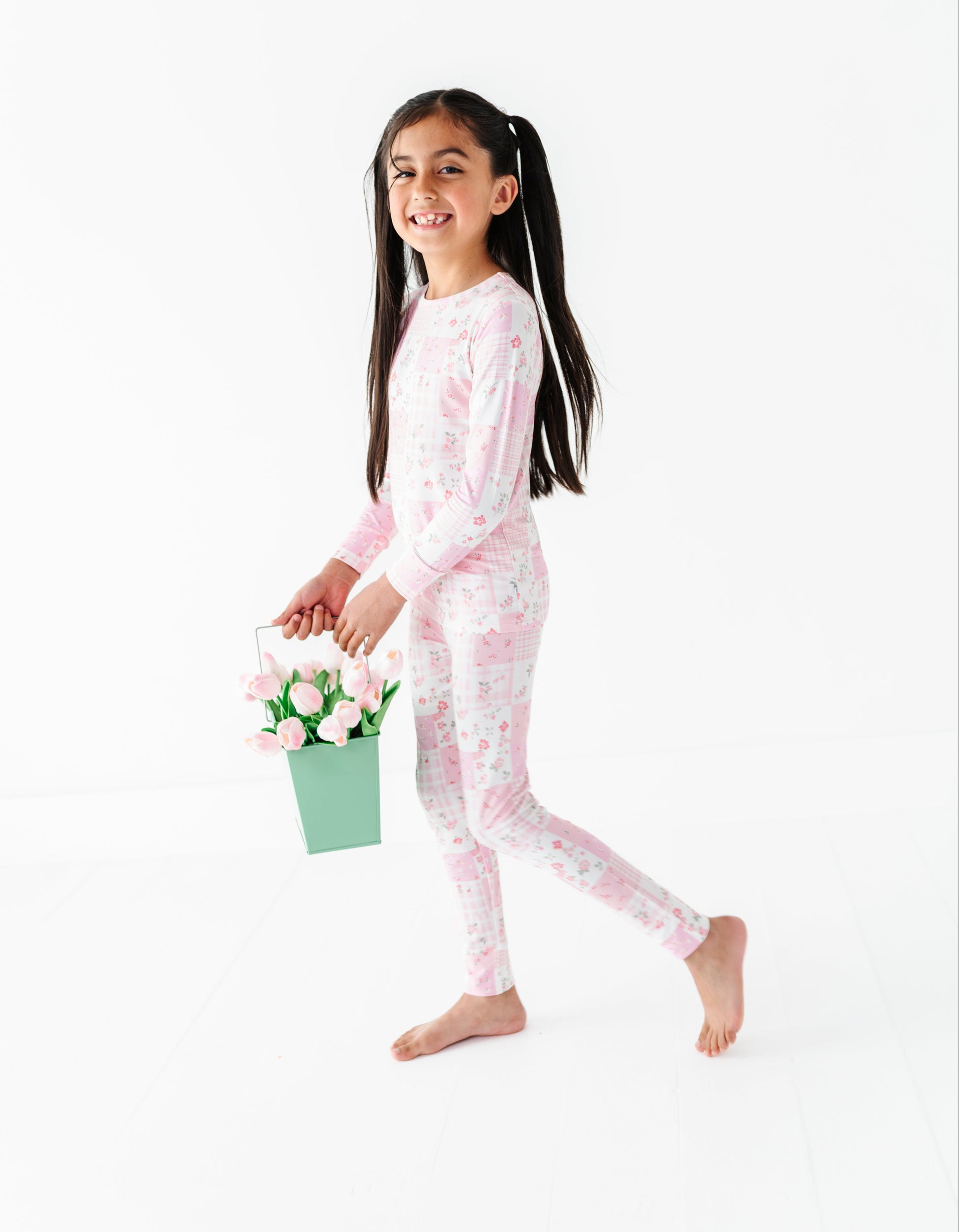 Young girl in pink floral bamboo two-piece pajamas holding a bucket of flowers on a white background