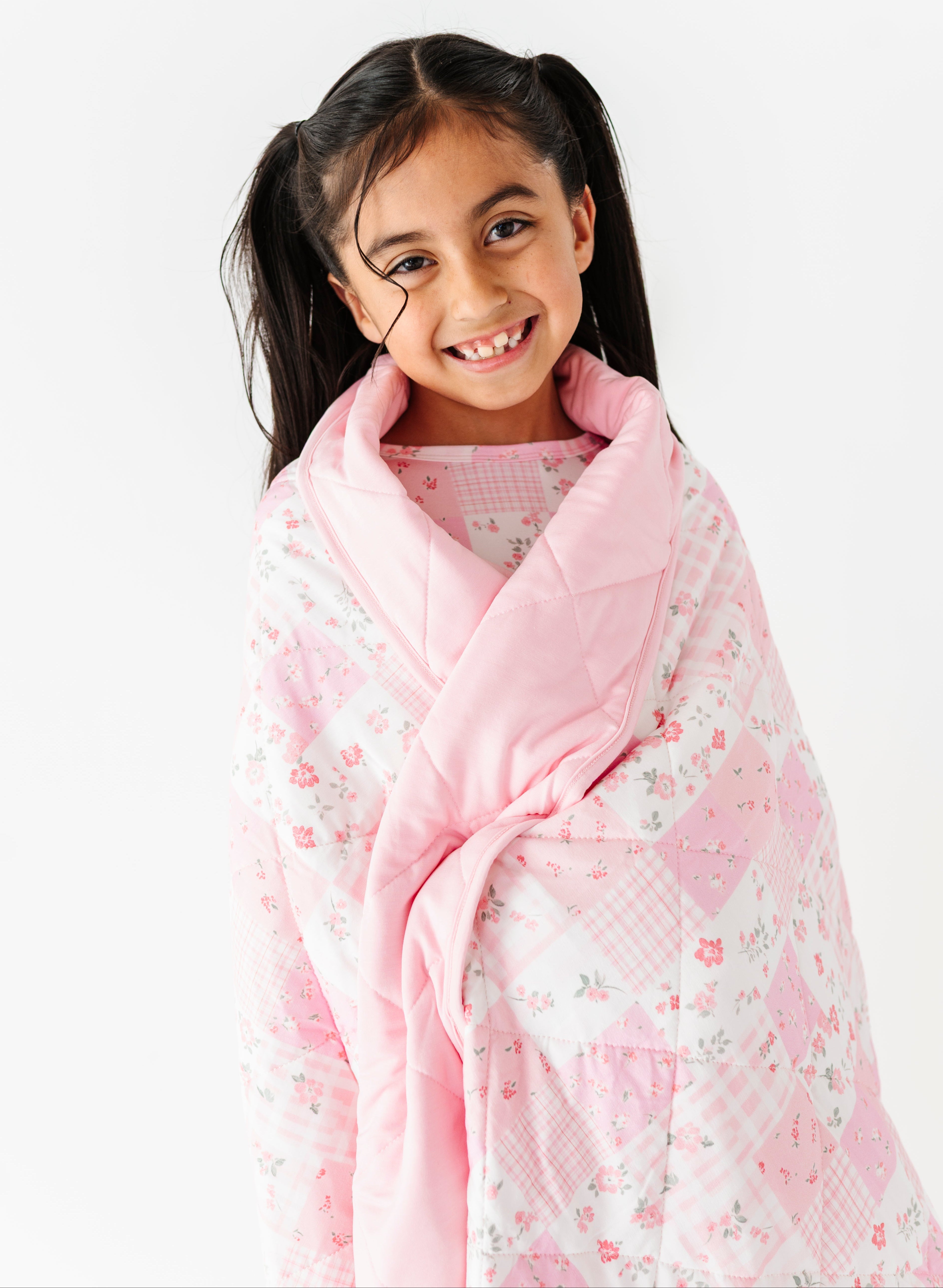 Young girl wrapped in a pink floral bamboo quilted blanket on a white background