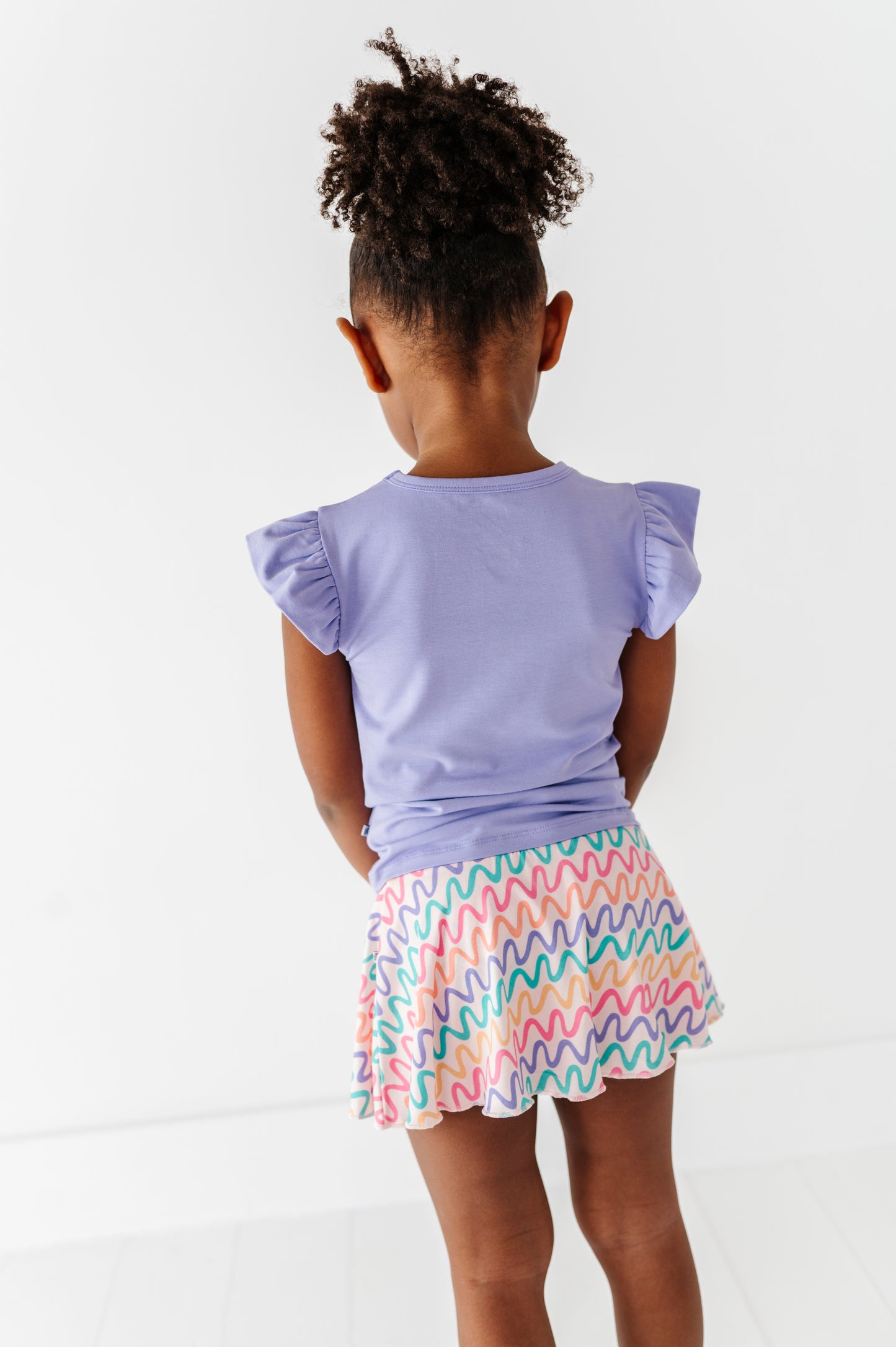 Child wearing a purple bamboo/cotton top and colorful bamboo skort on a white background