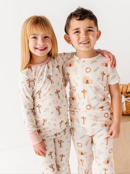 Two children wearing bamboo Easter pajamas with a pattern of crosses and animals on a white background.