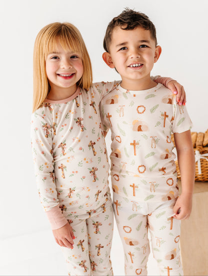 Two children wearing pajamas with a pattern of crosses and animals on a white background.