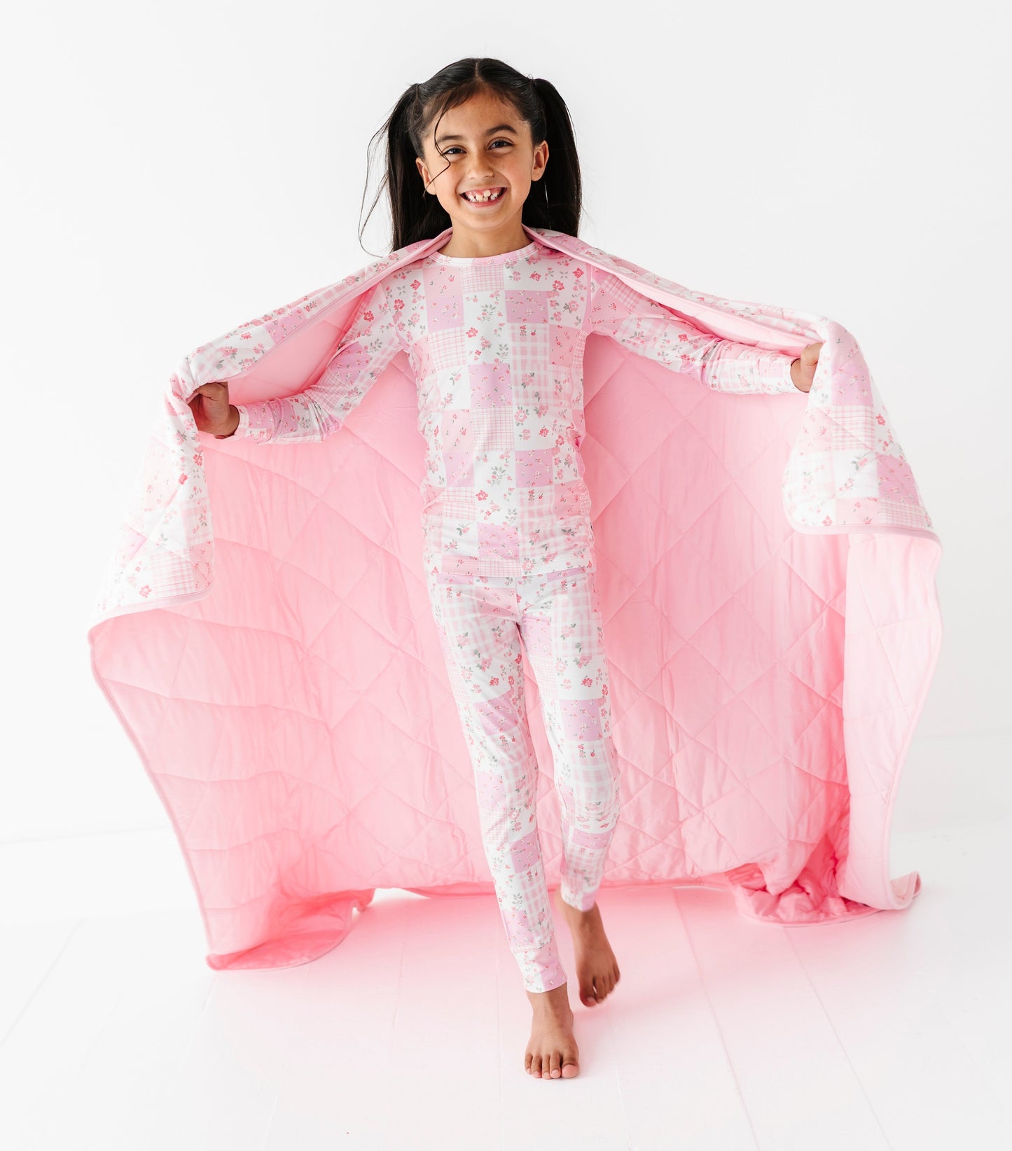 Child wearing a pink and white floral bamboo pajama set with a pink blanket on a white background