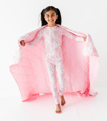 Child wearing a pink and white floral bamboo pajama set with a pink blanket on a white background