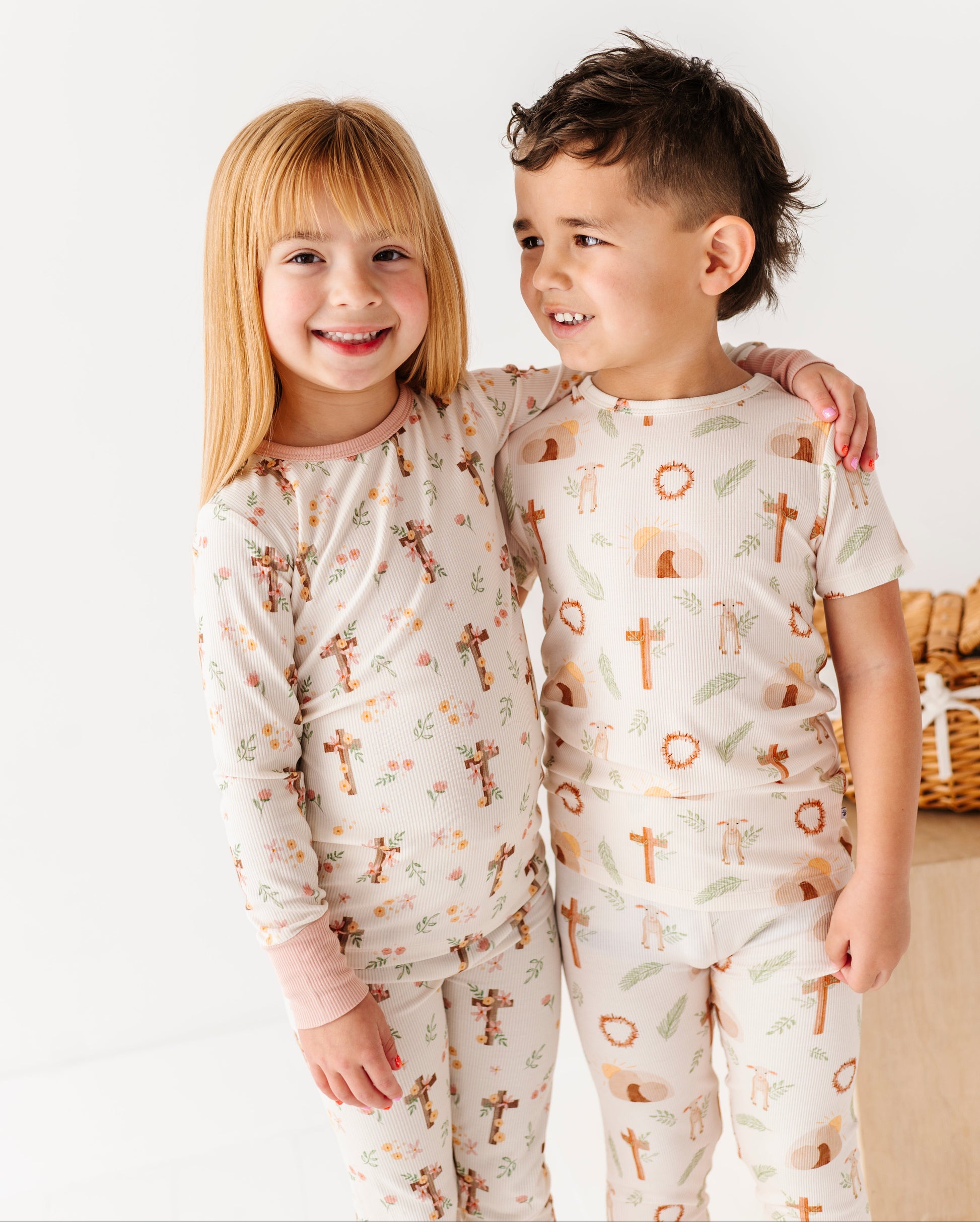 Two children wearing Easter pajamas with a pattern of crosses and animals on a white background.
