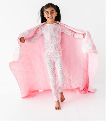 Child wearing a white and pink bamboo two-piece pajama set with a matching bamboo blanket on a white background