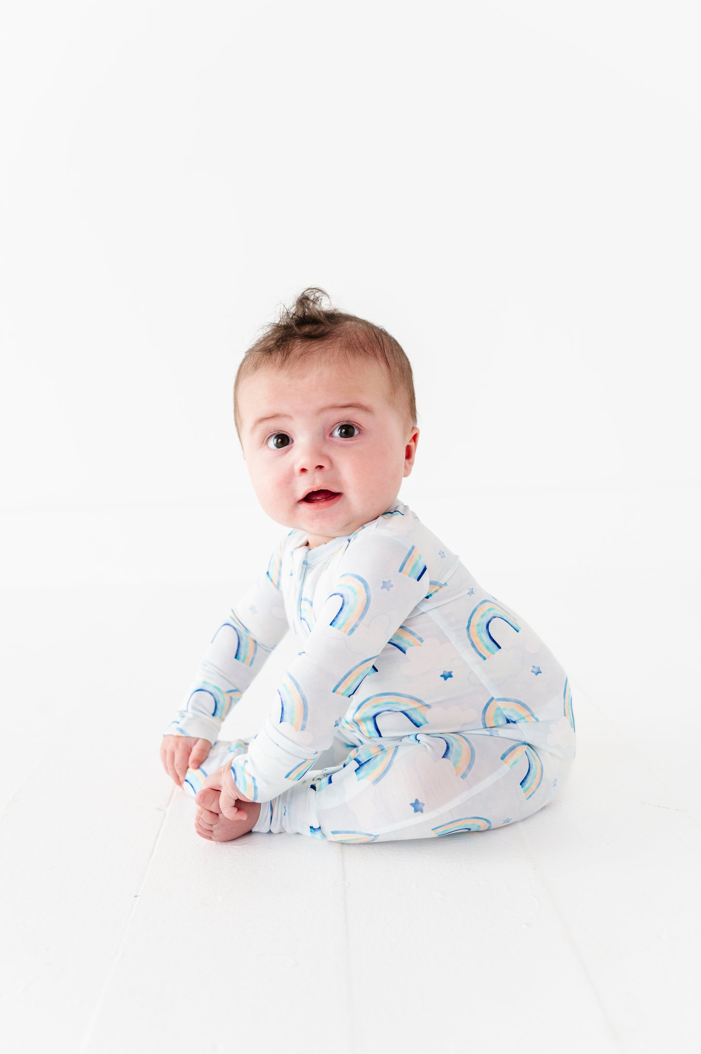 Baby wearing a bamboo zip romper with blue watercolor rainbow patterns on a white background