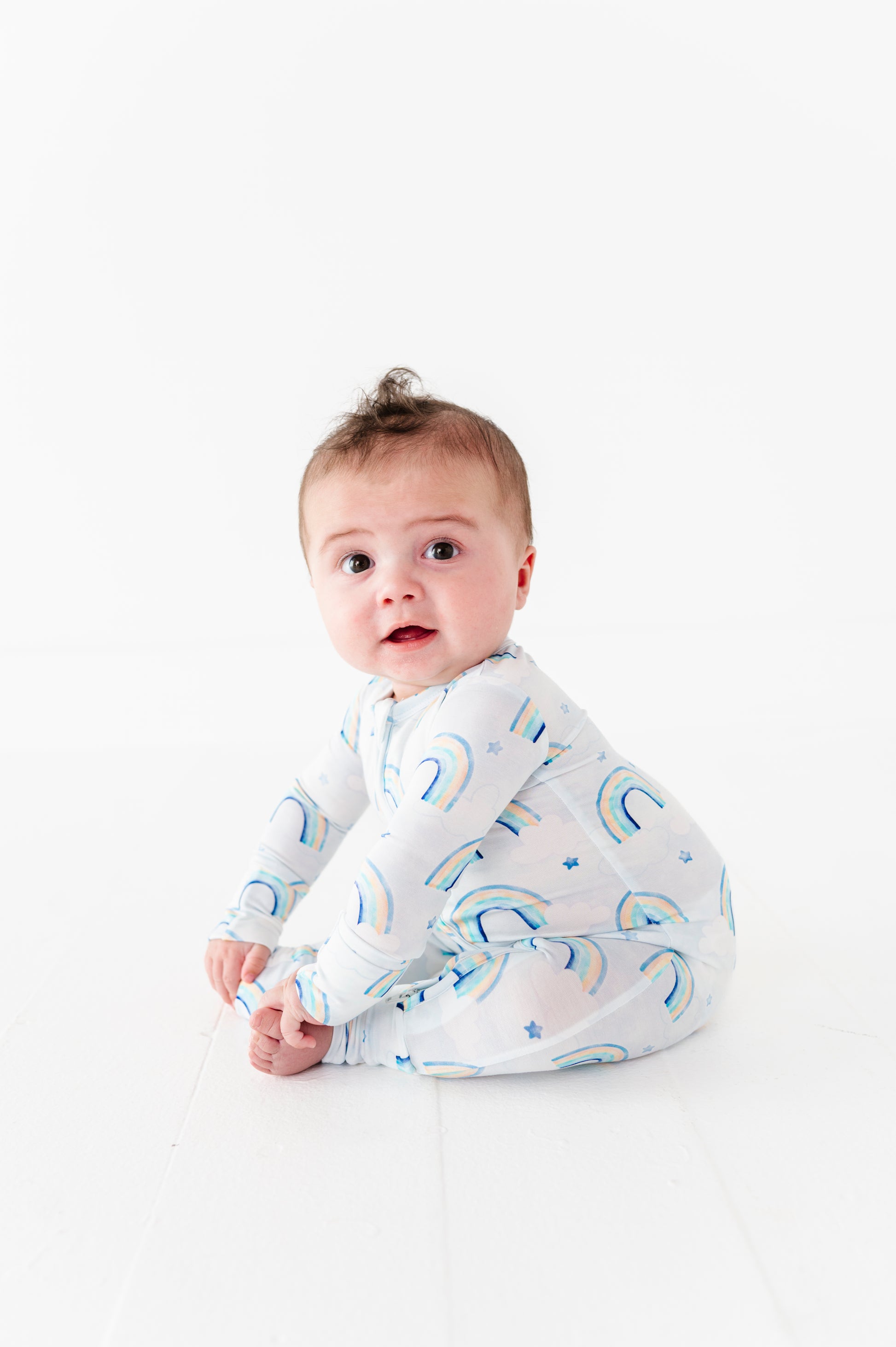 Baby wearing a bamboo zip romper with blue watercolor rainbow patterns on a white background