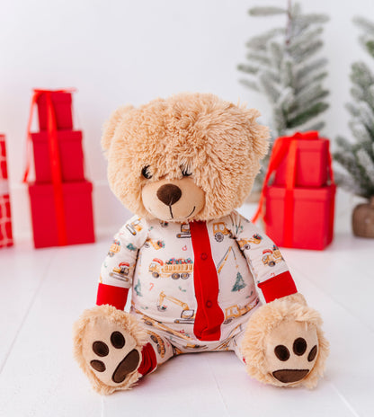 A light-colored teddy bear wearing a construction crew bamboo romper in a Christmas-themed room 