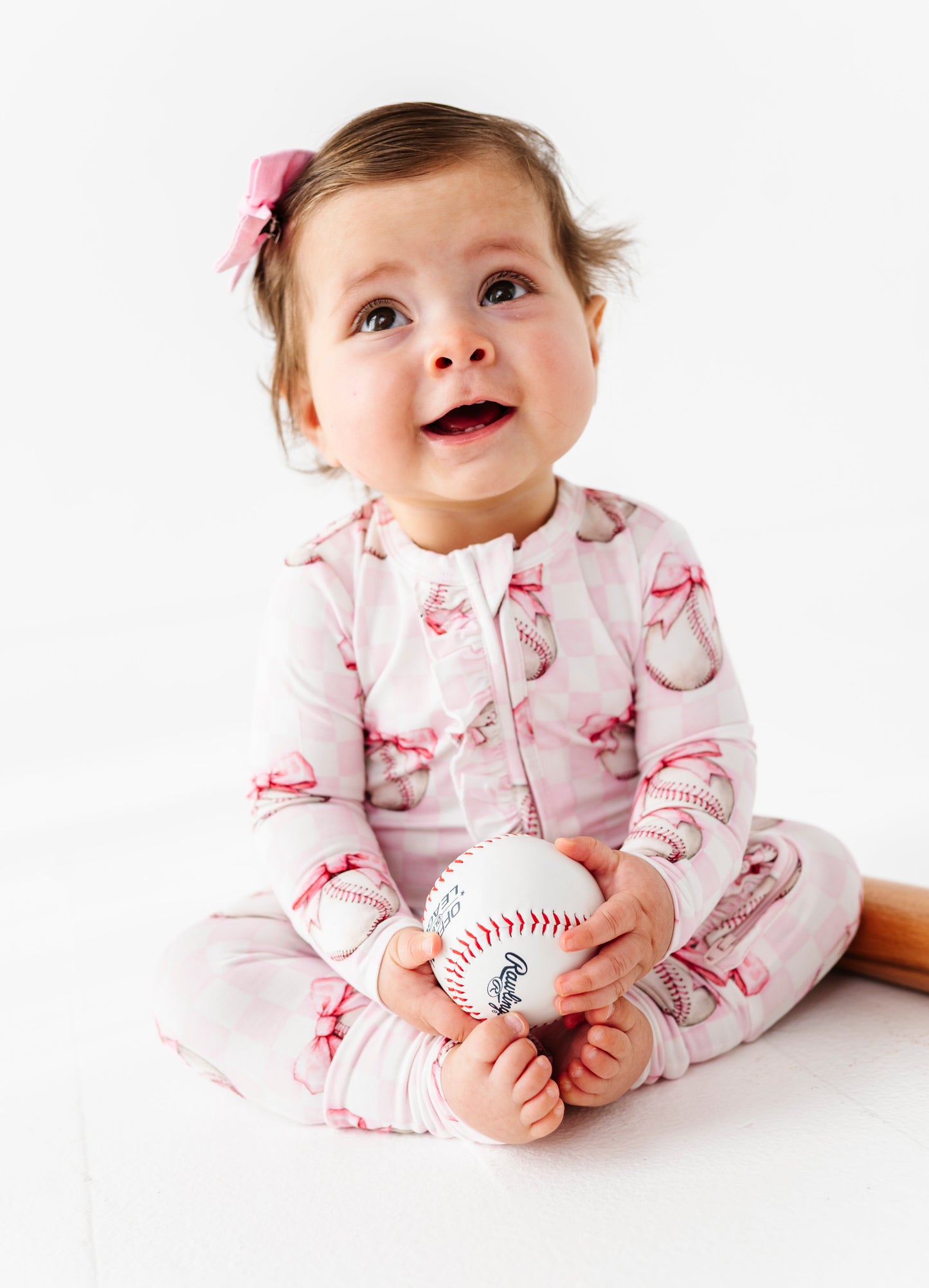 Baby holding a baseball wearing a pink and white bamboo convertible romper on a white background