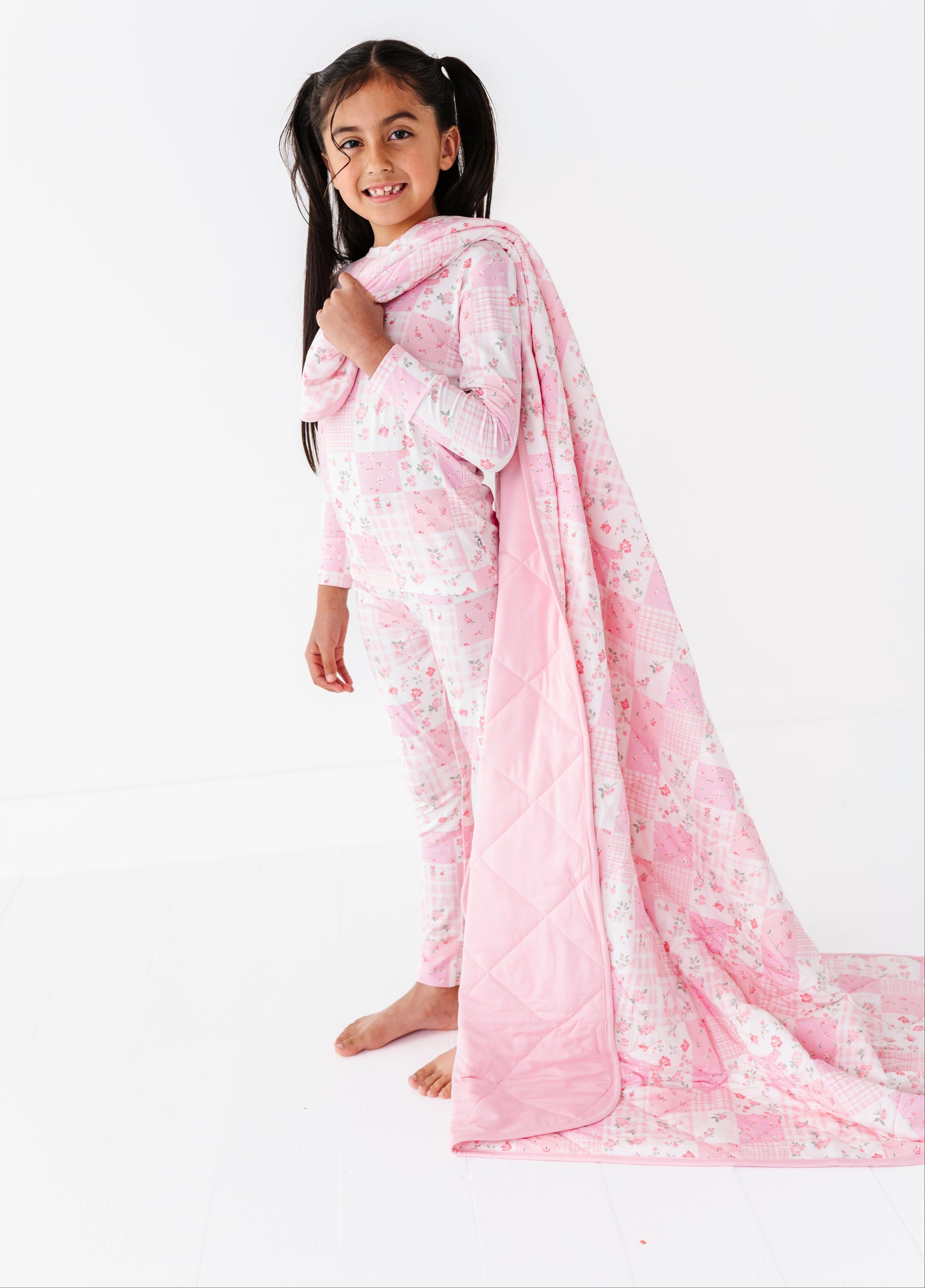 Child wearing pink bamboo two-piece pajamas with a matching blanket on a white background