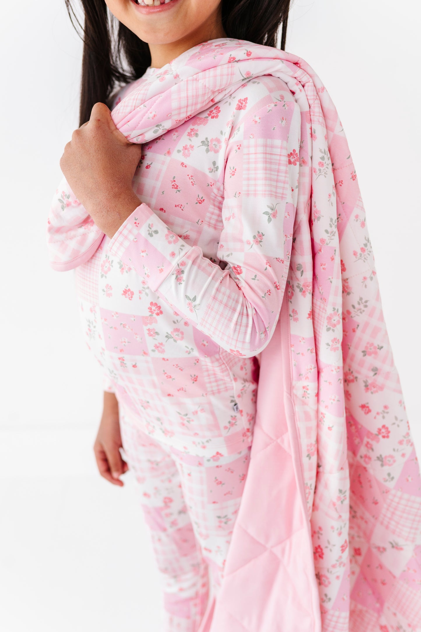 Child wearing a pink floral bamboo pajama set with a matching blanket  on a white background
