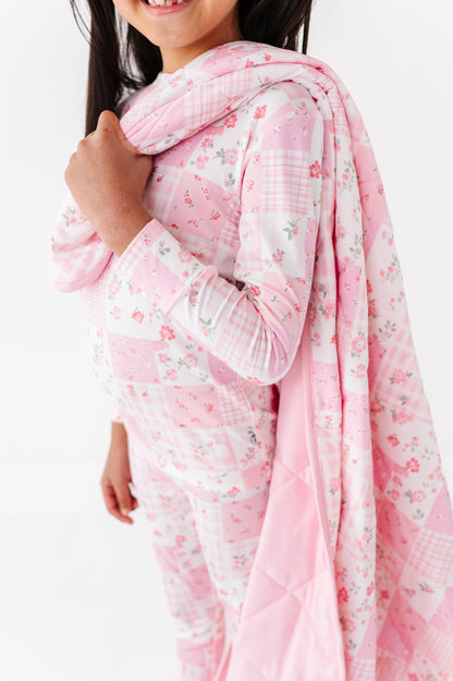 Child wearing a pink floral bamboo pajama set with a matching blanket  on a white background