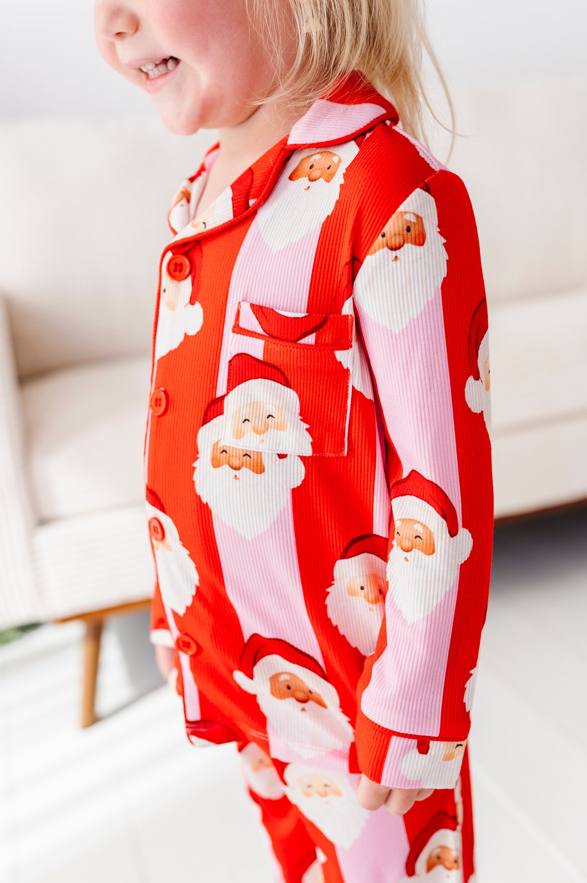 A child wearing red and pink bamboo pajamas with a Santa Claus face print, standing in a bright indoor room.