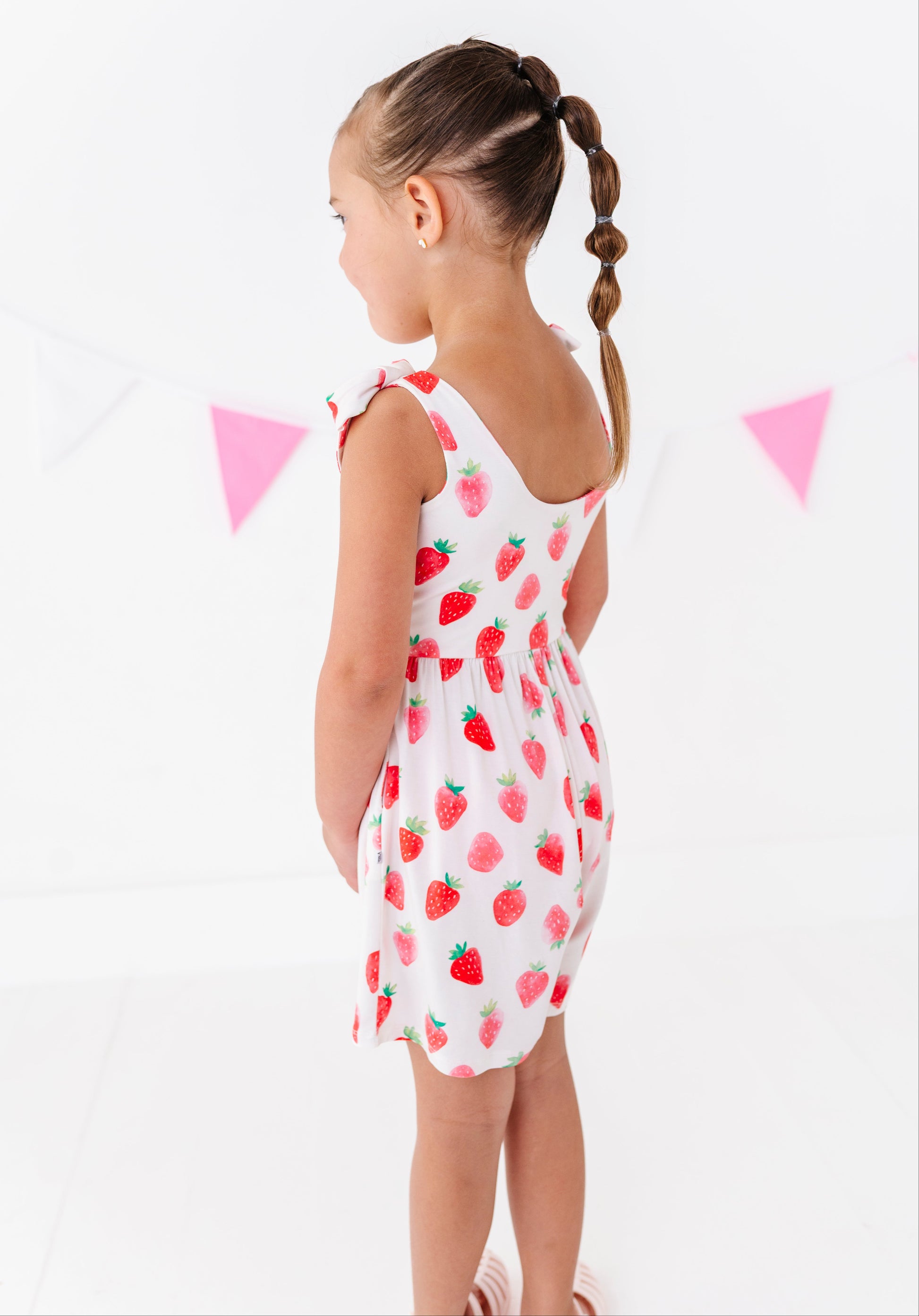 Young girl wearing a strawberry-patterned outfit on a white background with pink flags.