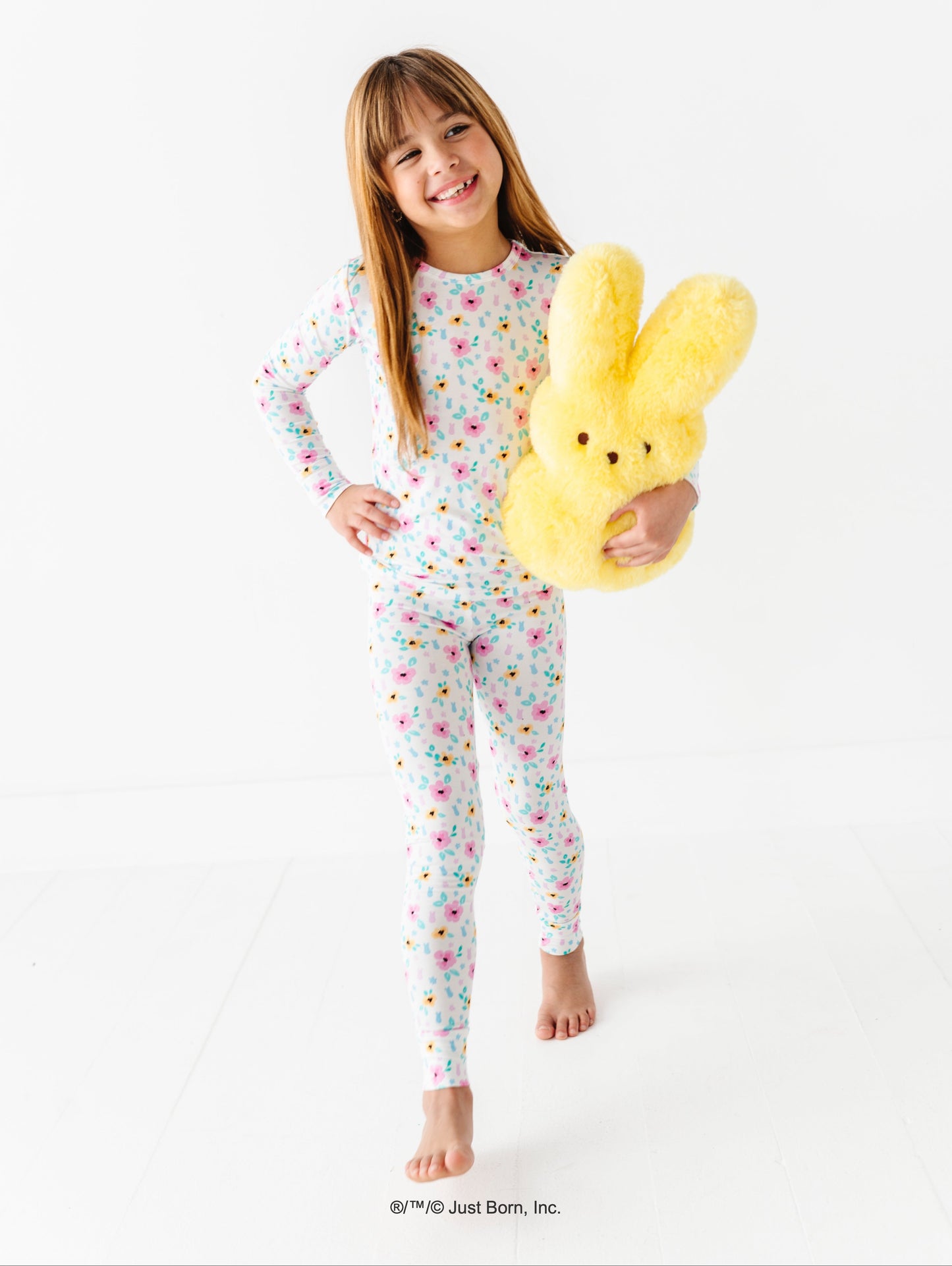 Child wearing a colorful floral PEEPS® pajama set holding a yellow plush PEEPS® toy on a white background