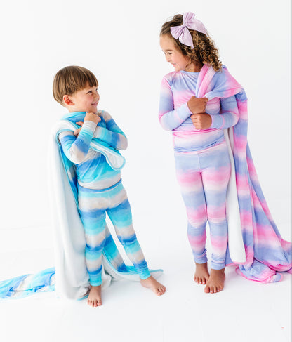 Two children wearing colorful striped bamboo pajamas with matching blankets on a white background