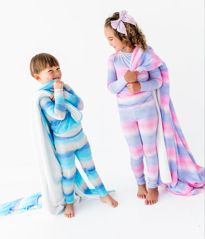 Two children wearing colorful striped bamboo pajamas with matching bamboo blankets on a white background